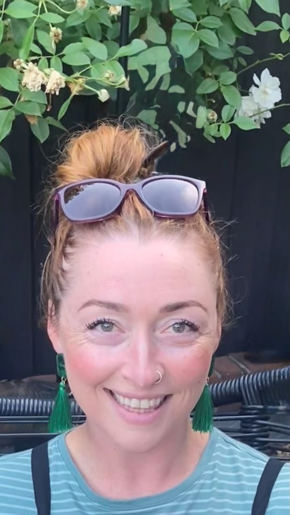 Smiling person outdoors with sunglasses and earrings.