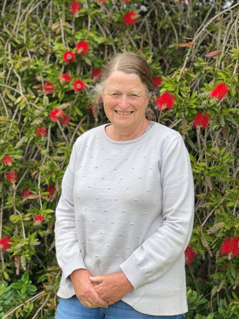 Smiling person in front of flowering bush.
