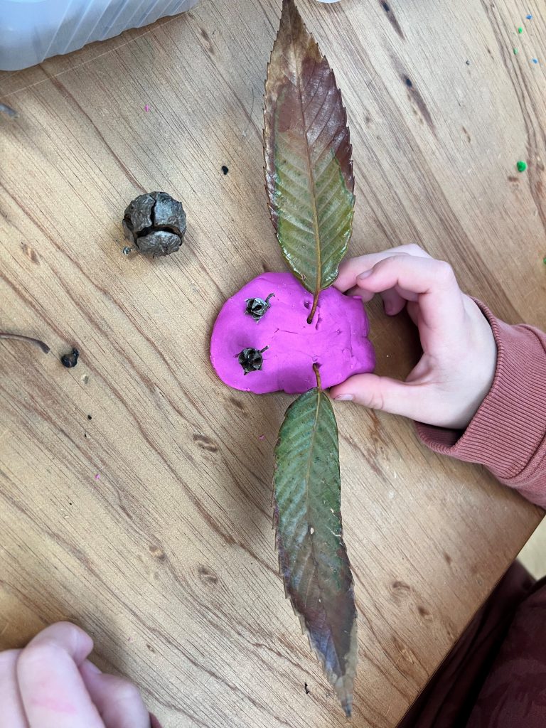 Child crafts face with leaves and seeds on clay.