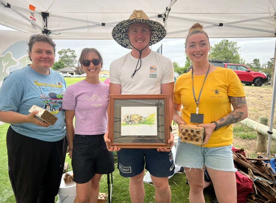 Group displaying framed artwork and bee habitats outdoors.